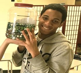 Student holding a large jar half full of many round balls